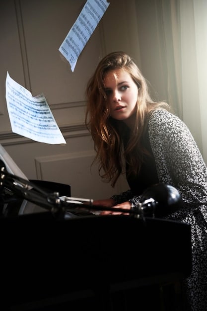 A songwriter sitting at a piano in a well-lit studio, with sheet music in front of them. The individual is in the midst of writing or composing, with a thoughtful expression on their face. The setting conveys creativity and the process of crafting original music content, emphasizing the importance of copyright protection for these unique creations.
