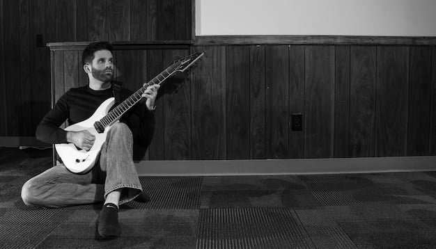 A black and white photo of a rock musician sitting alone in a dimly lit room, with a guitar resting against the wall. The musician appears to be deep in thought.