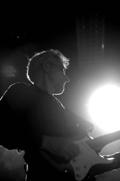 A black and white photo capturing a rock musician mid-performance on stage, their face filled with emotion, highlighted by the spotlight and energetic atmosphere of the concert.