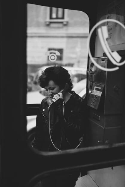 A black and white photo of a musician sitting alone on a tour bus, looking out the window with a distressed expression. Luggage and equipment are scattered around, emphasizing the chaotic and isolating nature of touring life.