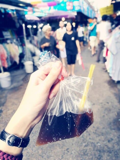 A person holding a small, clear plastic bag containing cash. The background is blurred and depicts common concert activities, like waiting in line or purchasing merchandise.