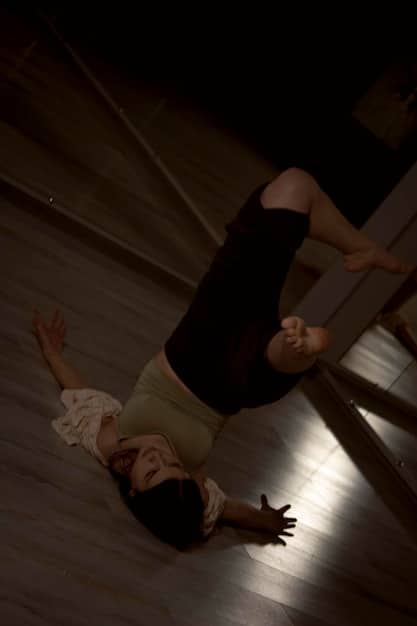 A person stretching their legs and back in a dimly lit room, focusing on muscle recovery after attending a concert.