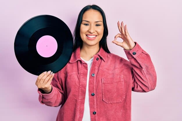 A close-up shot of a person holding a vinyl record towards a band member, with a marker in hand, ready for an autograph. The band member is smiling and engaging with the fan.