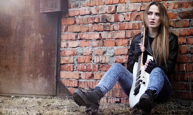 A person wearing a black band tee, ripped black skinny jeans, and black combat boots. They are holding a guitar, with a backdrop of a dimly lit stage. The focus is on the classic rocker outfit.