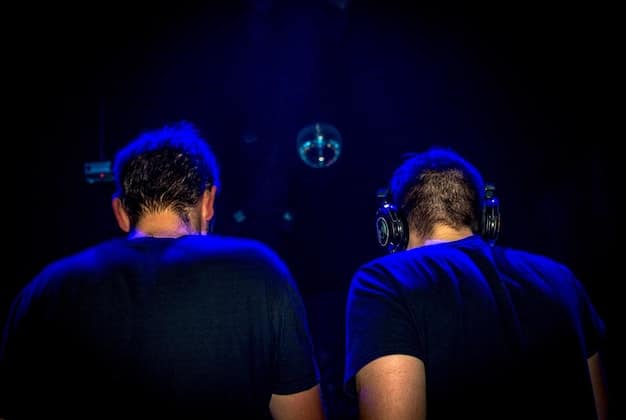 A pair of high-fidelity earplugs being inserted into someone's ears, with the concert stage lit up in the background, highlighting the importance of hearing protection during live music events.