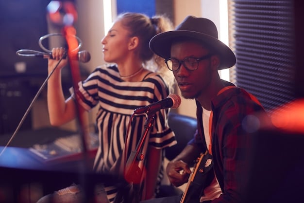 A recording studio scene with a young rock band recording their music. The lead singer is in a vocal booth, while the other band members are in the main room playing their instruments. A sound engineer is at the mixing console, adjusting levels and recording the performance. The atmosphere is creative and collaborative.