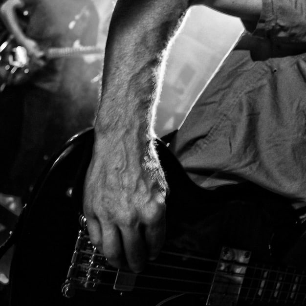 A close-up shot of a lead guitarist shredding on stage during a rock festival performance. The focus is on their hands and the guitar, with the blurred background revealing a massive crowd and stage lights. The image captures the intensity and skill of a live rock performance.