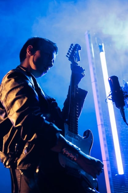 A dynamic shot of a lead guitarist captured from a slightly elevated position in a crowded concert, with blurred audience hands in the foreground and vibrant stage lights illuminating the performer.